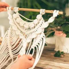 Mains créatives travaillant sur une décoration murale en macramé. Une belle idée déco macramé pour un intérieur bohème.