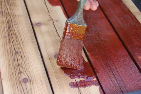 Application d'une couche de peinture rouge sur des planches de bois, comme pour repeindre des volets en bois.