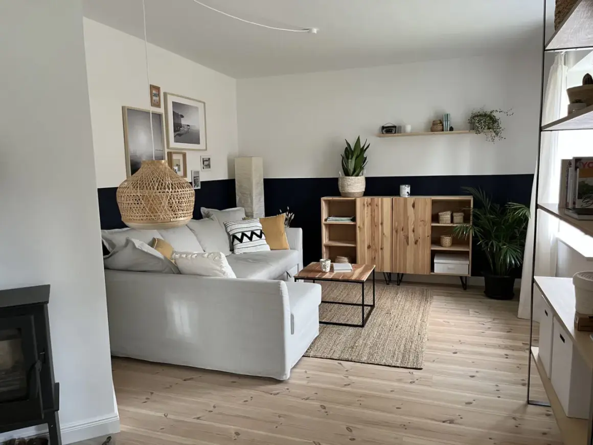 Salon moderne avec canapé gris, meuble en bois et tapis en jute. Le mur est peint en deux tons, blanc et bleu nuit, rappelant des techniques de peinture acrylique.
