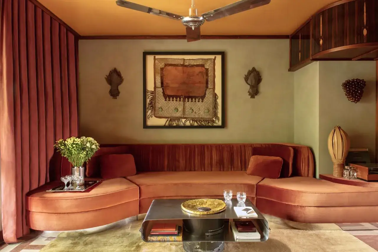 Canapé arrondi velours couleur terracotta, tableau ethnique, rideaux assortis, et un plafond orange.